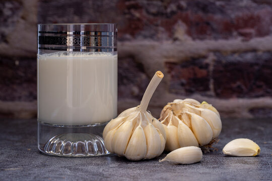 Hot garlic milk in a glass cup with peeled garlic on the background