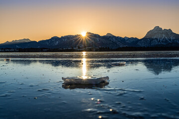 Eis am Hopfensee im Winter mit Sonnenaufgang und Bergen