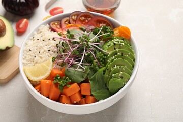 Delicious vegan bowl with avocados, carrots and microgreens on light grey table, space for text