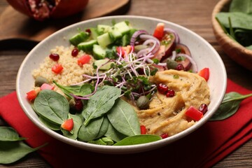 Delicious vegan bowl with cucumbers, spinach and bulgur on wooden table, closeup