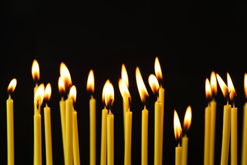 Many burning church candles on black background