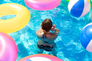 Inflatable life buoys in the pool of teenage girls in bikini and appears among inflatable balls.