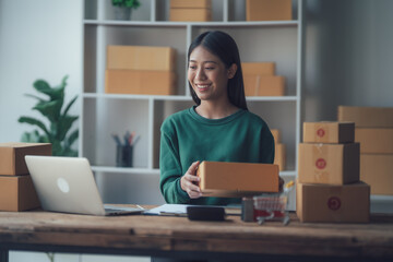 Startup small business entrepreneur or freelance Asian woman using a laptop with box, Young success Asian woman with her hand lift up, online marketing packaging box and delivery, SME concept.