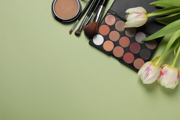 Obraz na płótnie Canvas Flat lay composition with eyeshadow palette and beautiful flowers on pale olive background, space for text