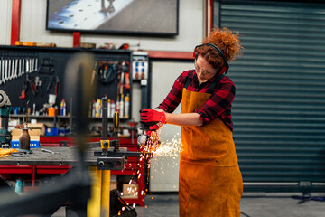 A self-employed worker is cutting a metal beam using a grinder, she is focused on her work and...