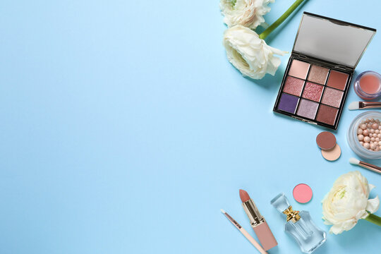 Flat lay composition with different makeup products and beautiful flowers on light blue background. Space for text