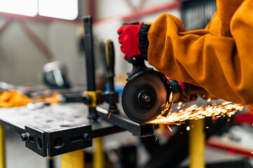 Close-up of a woman in STEM using grinder to cut a metal bar, wearing gloves and protective sleeves...