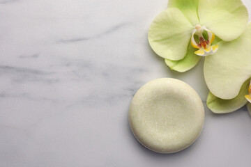 Fototapeta na wymiar Solid shampoo bar and orchid flowers on white marble table, flat lay with space for text. Spa composition