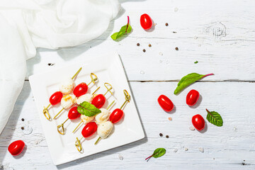 Fototapeta na wymiar Traditional healthy Italian appetizer. Mozzarella, fresh leaves and cherry tomatoes on skewers