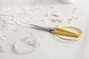 Pair of scissors, beautiful lace and beads on white table, closeup