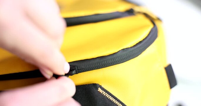 Person closes black padlock on yellow fabric backpack closeup. Quality zipper on bag