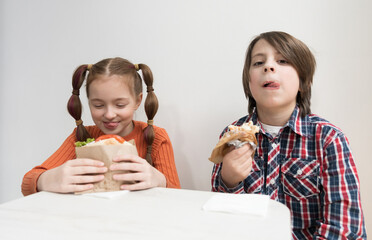 Hungry little kids eating Greek fast food for lunch. 9 year old girl with ponytails and 11 year old boy in plaid shirt enjoying sandwiches in a cafe
