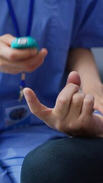 Vertical video: Assistant doing insulin level measurement with instrument to help senior sick man with diabetes, using glucometer to check glucose and sugar from blood. Patient attending checkup visit