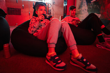 Two boys gamers play gamepad video game console in red gaming room.
