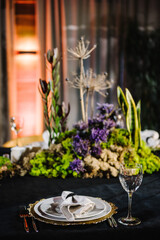 Wedding reception. Rustic. Composition of bark tree, wooden decor, moss in restaurant. Table decorated plates and glasses, candles, flowers, greenery. Interior of table for guests with natural decor.