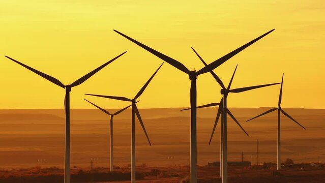 Silhouettes windmills large orange sun disc summer lens flare. Alternative energy. Large wind turbines close up with blades in field aerial view bright orange sunset wind park slow motion drone turn