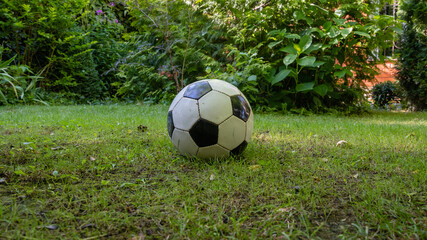 Soccer ball lies on lawn in garden. Close-up. Grass on lawn for playing football. Soccer ball stitched with white and black hexagons.