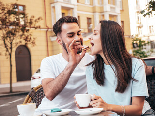 Smiling beautiful woman and her handsome boyfriend. Happy cheerful family. Couple drinking coffee in restaurant. They drinking tea at cafe in the street. Holding cup. Feeding his girlfriend