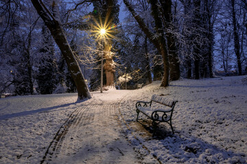 Winter park alley at dusk with bench under street lamp