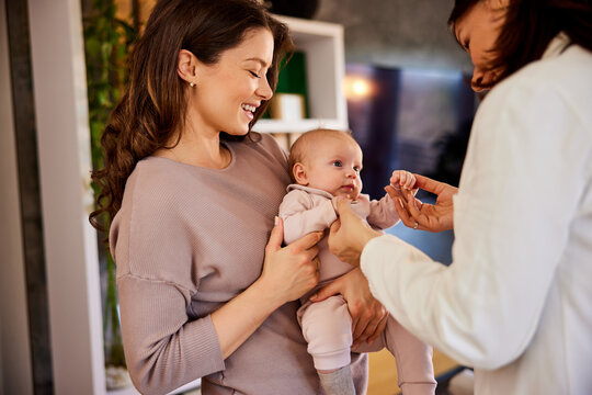 A Female Pediatrician Entertains A Cute Baby In Her Mother's Arms During A Home Visit.