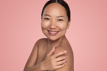 Positive young ethnic lady touching shoulder and smiling in studio