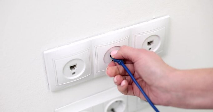 Closeup of woman hand takes out network cable from socket in wall. Blocking and turning off home internet