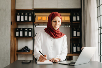 Young Arabic female entrepreneur wearing a hijab working online with a laptop at office