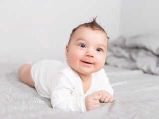 The baby lies on his stomach on the bed. A beautiful baby smiles. Mockup for advertising, design, celebration, postcards.