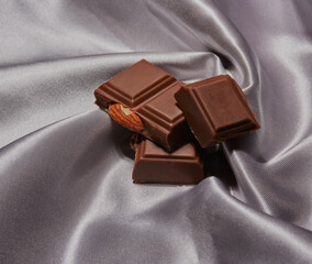 Pieces of fruit and nut chocolate stacked on some swirling silk.