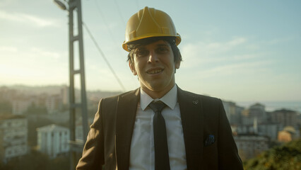 A Young, Handsome, Suit-and-Tie-Clad, Beardless, Helmeted Businessman or Urban Planner Smiling at the Camera with a Cityscape Background