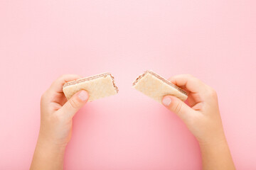 Little girl hands holding broken wafer pieces on light pink table background. Pastel color. Sweet...