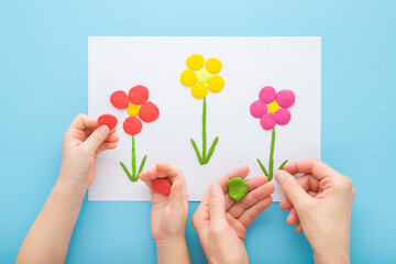 Adult mother and child hands modeling colorful flowers from clay on white paper on blue table...
