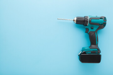 Dark black green professional battery driver drill on light blue table background. Pastel color....