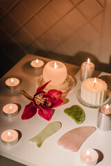 Gua sha tool. Candles, and orchid flowers on table. Facial massage for lifting, face therapy, home spa, mockup. Skincare concept. Cosmetology, body massage, spa procedure. Details decor in spa salon.