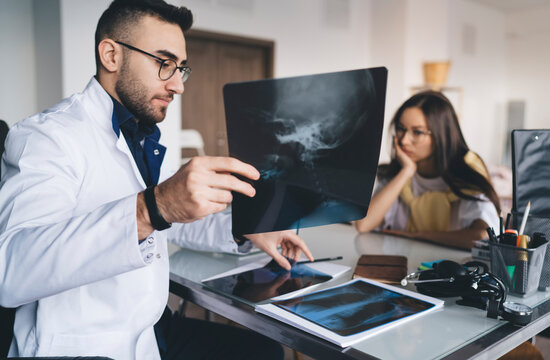 Focused male doctor showing neck x ray image to upset patient