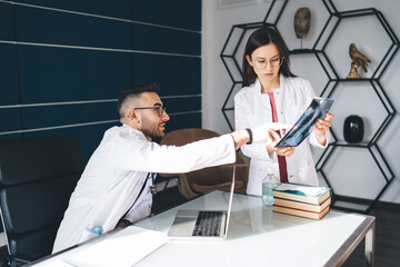 Serious young woman doctor standing with film near table with books