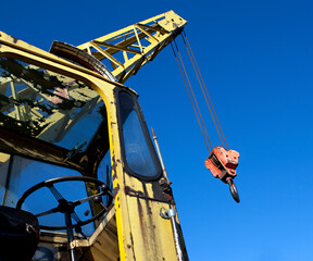 Fototapeta premium Old yellow battered crane with boom and hook against the blue sky.