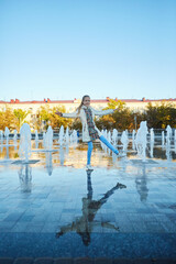 A girl in warm clothes walks down between the jets of the fountain.