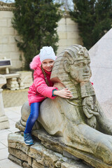 A girl is sitting on a small sculpture of the sphinx.near a replica of the Egyptian pyramid in the...
