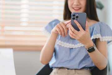 In a cozy living room at home, a beautiful young woman engrossed in messaging on her smartphone...