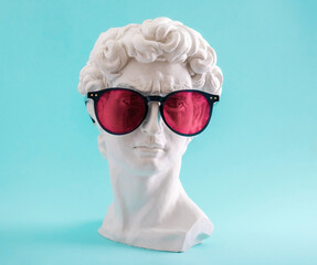 Plaster statue head wearing pink sunglasses on blue background.