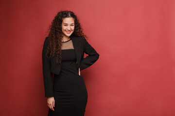 fashion female portrait. Girl, curly girl with black hair in a strict business suit on a red, pink background. High quality photo