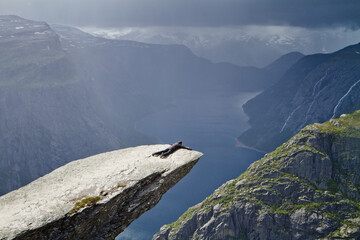 Man lies on Trolltunga rock (Troll's Tongue rock) and makes the photo with the Norwegian mountain landscape