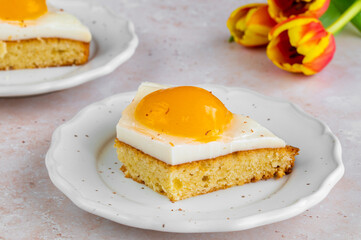 Homemade German Fried Eggs Cake Spiegeleierkuchen with apricot and milk pudding on a light background with tulips. Traditional Easter Dessert. Festive Easter food.