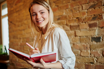 Smiling young woman studying and taking notes in cafeteria