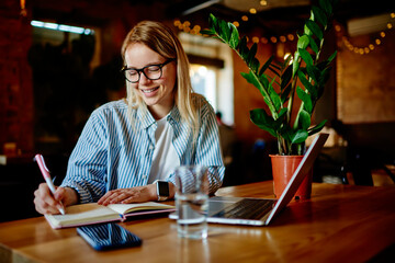 Woman taking notes in notebook at cafe table with gadgets