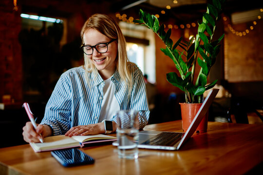 Woman taking notes in notebook at cafe table with gadgets