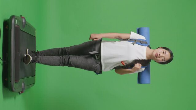 Full Body Of Asian Female Hiker With Mountaineering Backpack Looking Around While Walking On A Treadmill On Green Screen Background In The Studio
