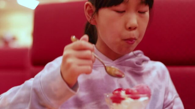 外食先の店で楽しくいちごパフェを食べる小学生の女の子の様子
