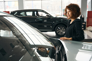 Fototapeta na wymiar Smiling multiracial woman put her hand on hood of anew car
